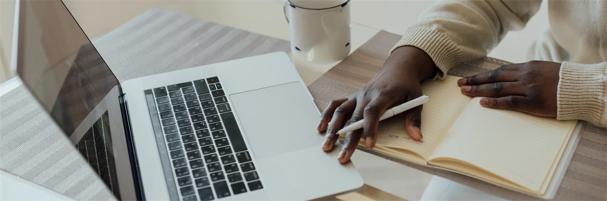 Dator i silver med hand som håller i en vit penna. 