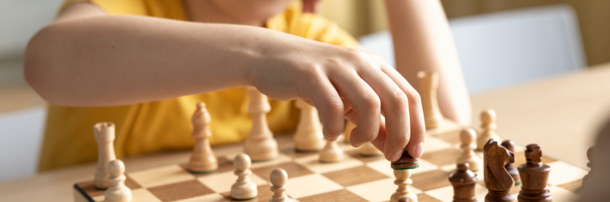 En pojke med brunt hår och gul tröja spelar schack 