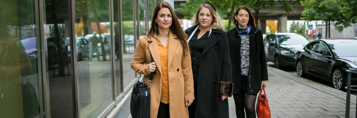 Tre kvinnor i ytterkläder står på trottoar
