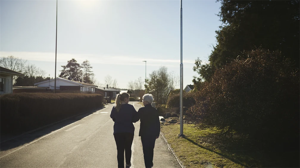 En äldre kvinna håller armkrok med en kvinna ute på promenad.