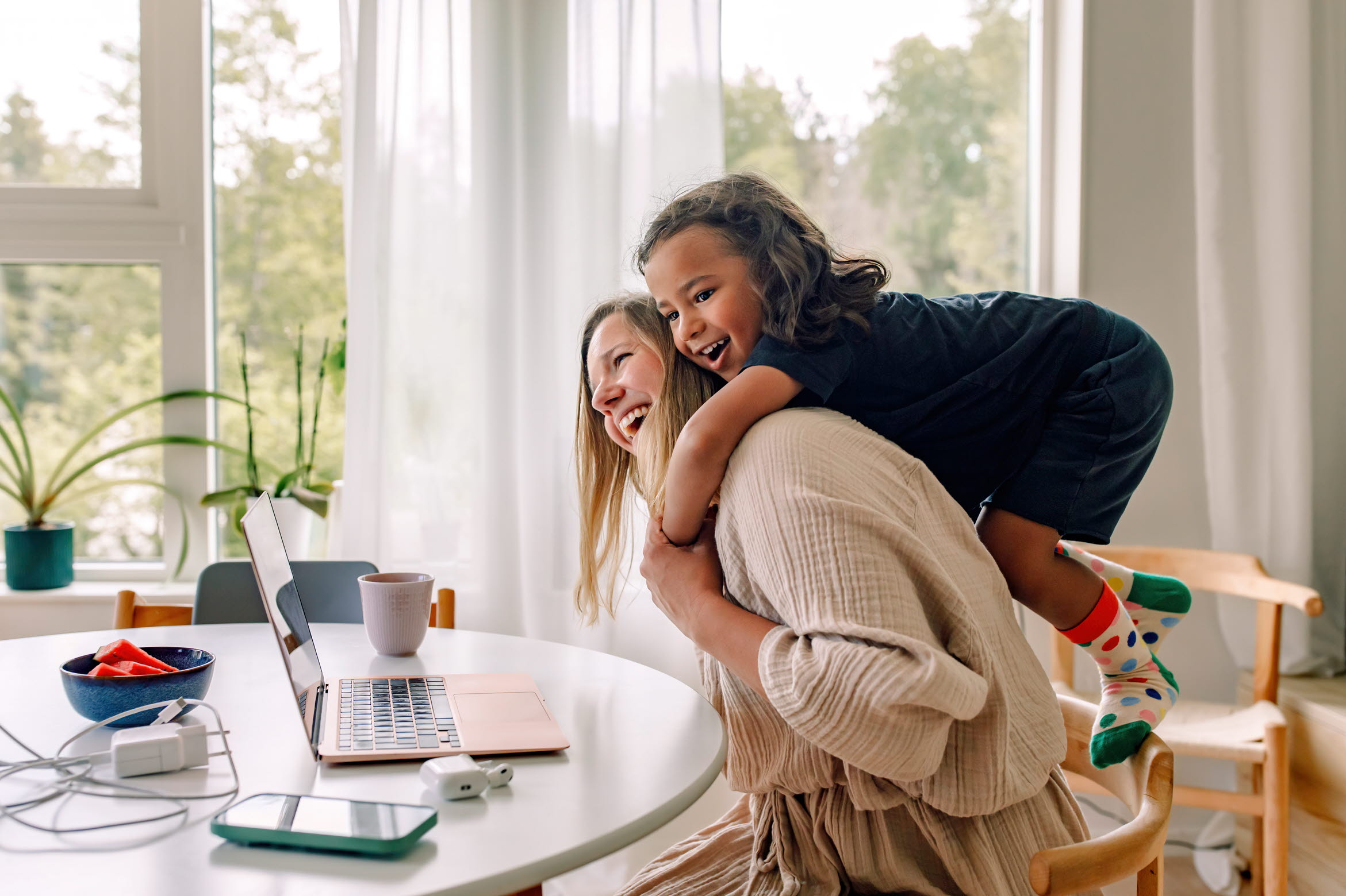Jente klemmer kvinne i en hyggelig stue, kvinnen jobber på datamaskin