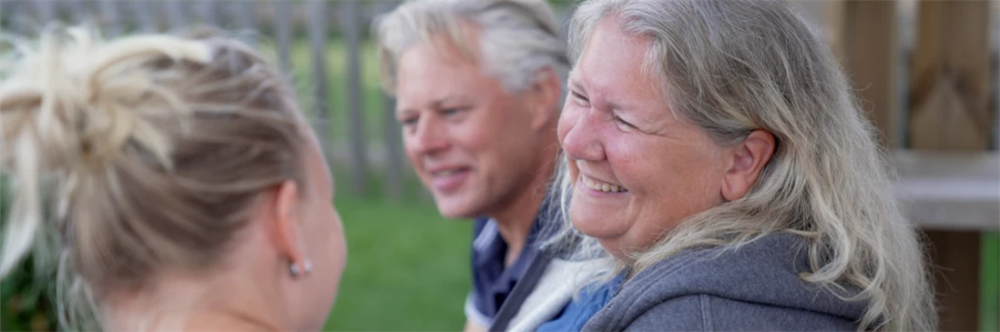 Kvinna ler mot en ung tjej. Man som skrattar med i bakgrunden. Sommarkänsla. 