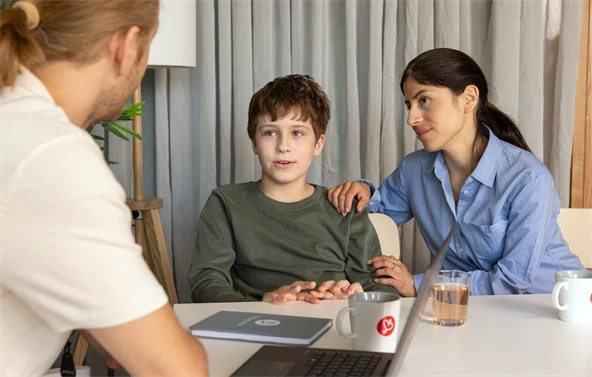 Lapsi istuu pöydän ääressä kahden aikuisen kanssa.