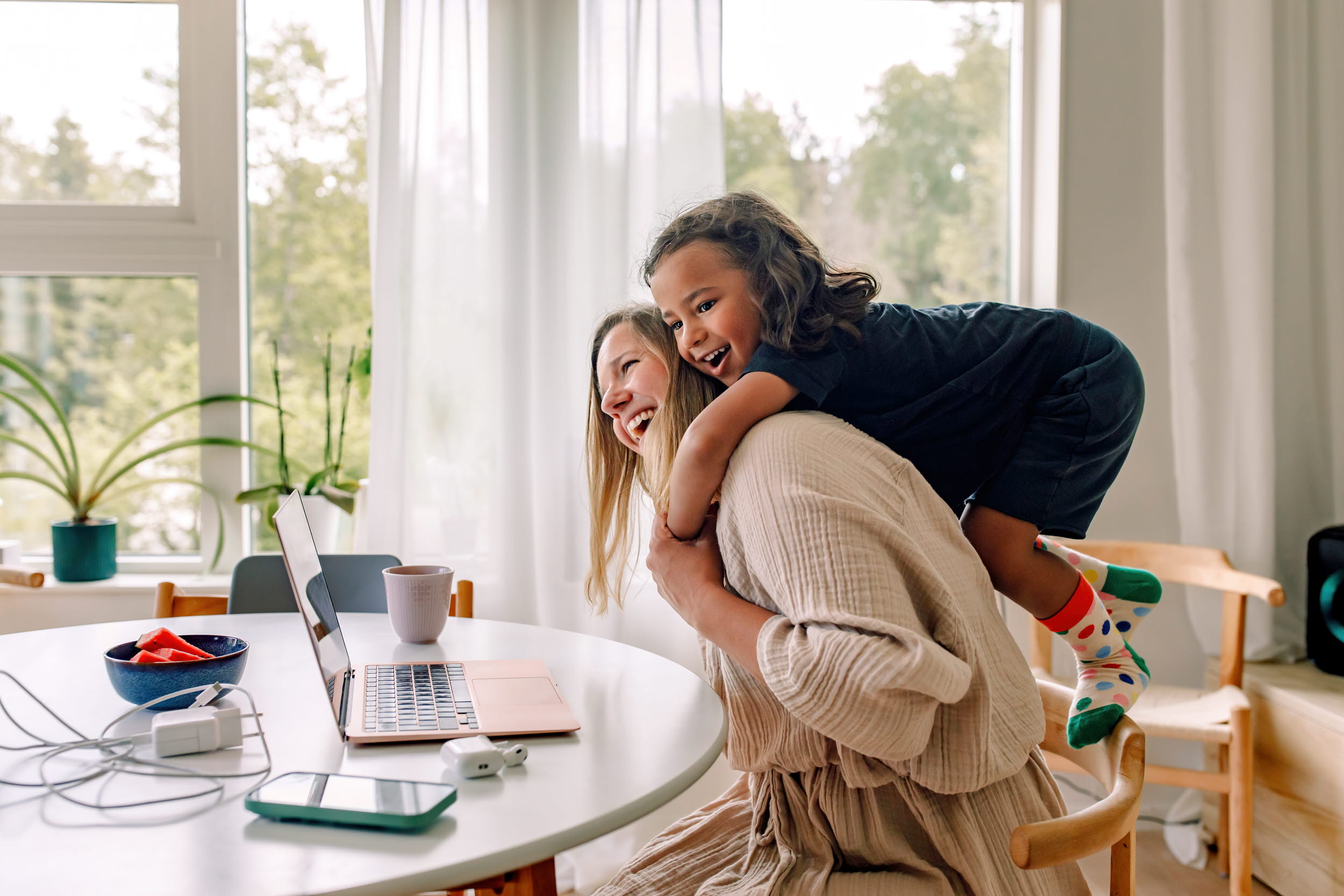 Jente klemmer kvinne i en hyggelig stue, kvinnen jobber på datamaskin