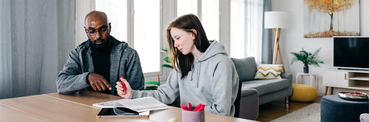 Kaksi henkilöä pöydän ääressä opiskelemassa.