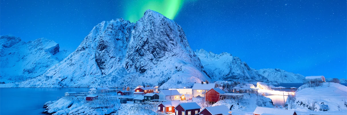Hus i Lofoten i Nord-Norge foran fjell med nordlys på himmelen