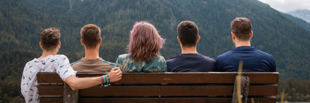 Män och en kvinna som sitter på en bänk och tittar ut över ett berg. 