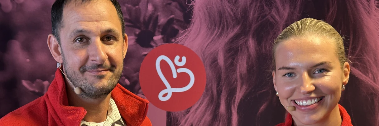 Michael og Kristin står foran rosa Humanabakgrunn og smiler til kameraet