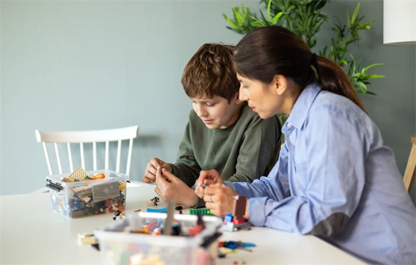 En kvinna och en pojke sitter vid ett bord och leker med lego