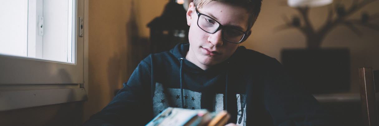 En pojke med glasögon och hoodie sitter och tittar på några böcker. 