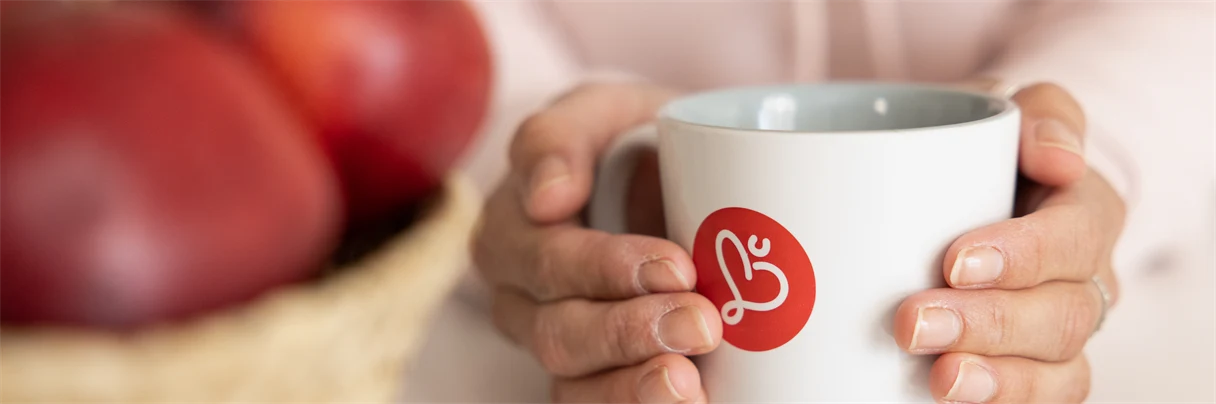 Kaffekopp med Humana logotyp på två händer håller runt koppen