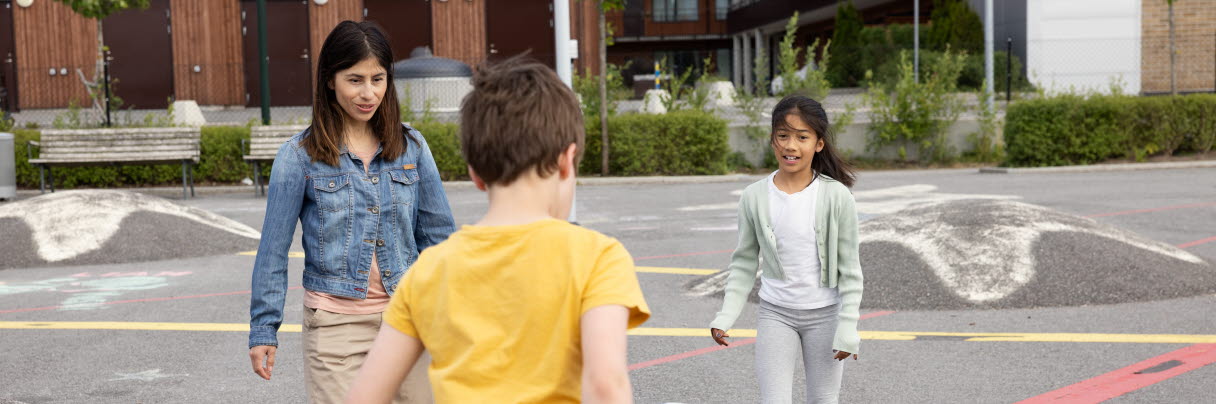 En kvinna, en flicka och en pojke, spelar fotboll på en asfaltsplan