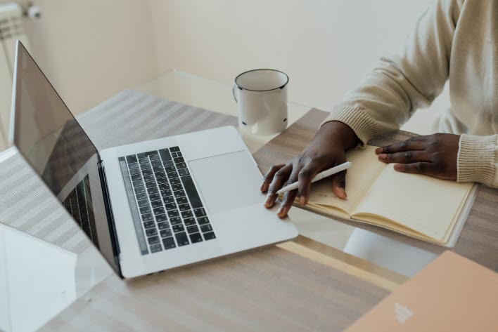 Dator i silver med hand som håller i en vit penna. 