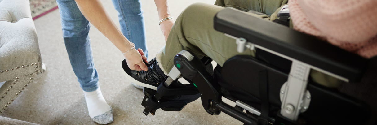 assistent hjälper en person i rullstol med skorna