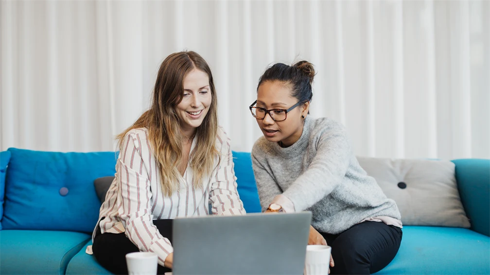 två kvinnor i en soffa som diskuterar vad som händer på datorn