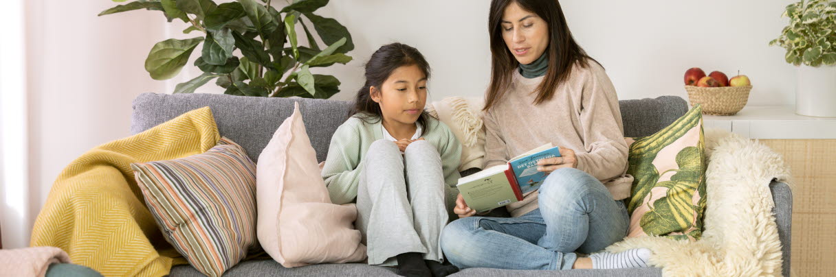 En kvinna och en flicka läser bok i en soffa