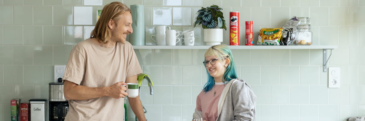 En man och en ung kvinna står i ett kök och samtalar, de är glada