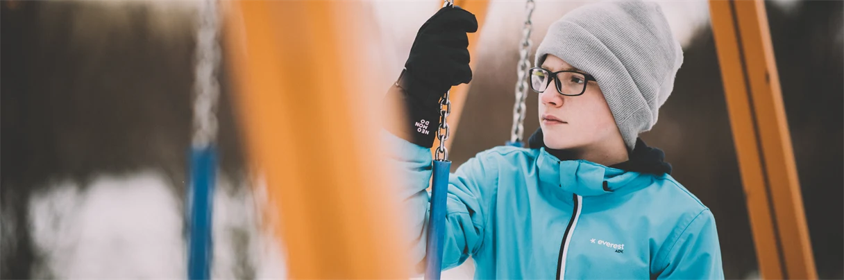 The boy is standing under a swing.
