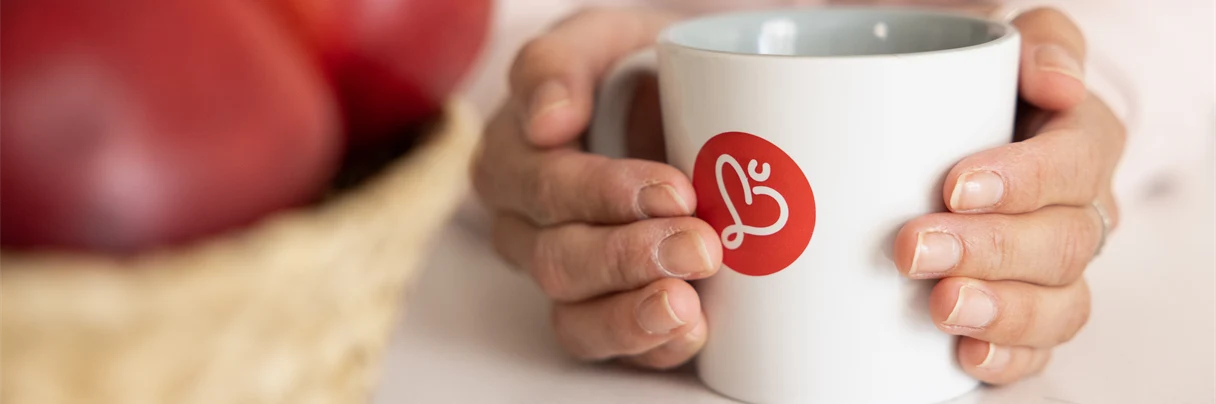 Kaffekopp med Humana logotyp på två händer håller runt koppen
