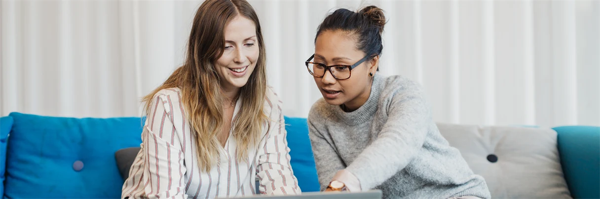 två kvinnor i en soffa som diskuterar vad som händer på datorn