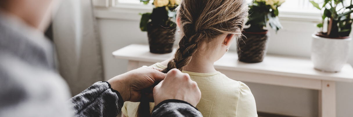An adult braids a girl's hair.