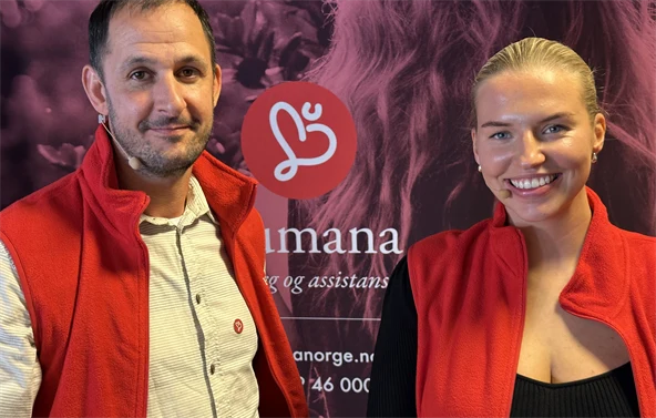 Michael og Kristin står foran rosa Humanabakgrunn og smiler til kameraet