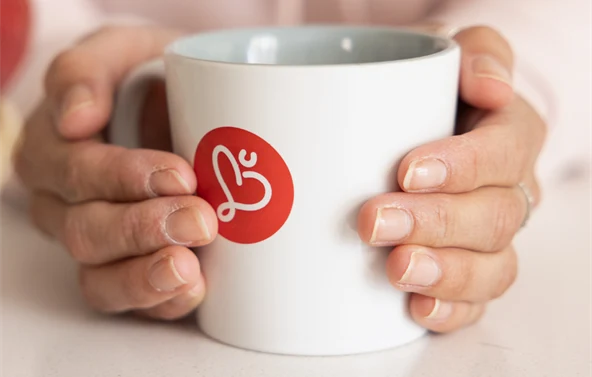 två händer som håller i en kopp med humanalogga på