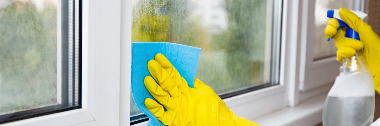 Hender med gummihansker på vasker vinduer