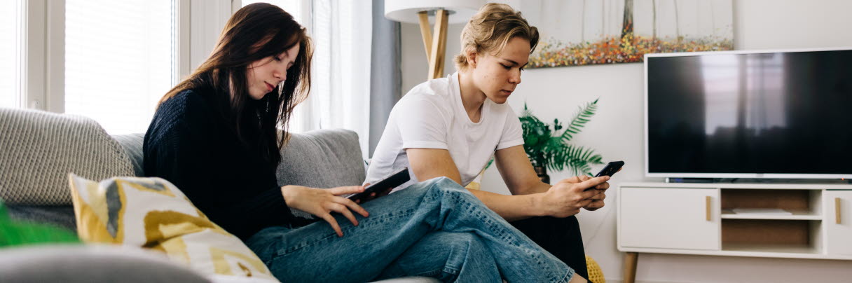 A girl and a boy are sitting on the couch with a tablet and a cell phone