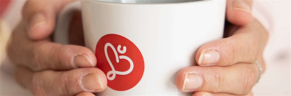 två händer som håller i en kopp med humanalogga på